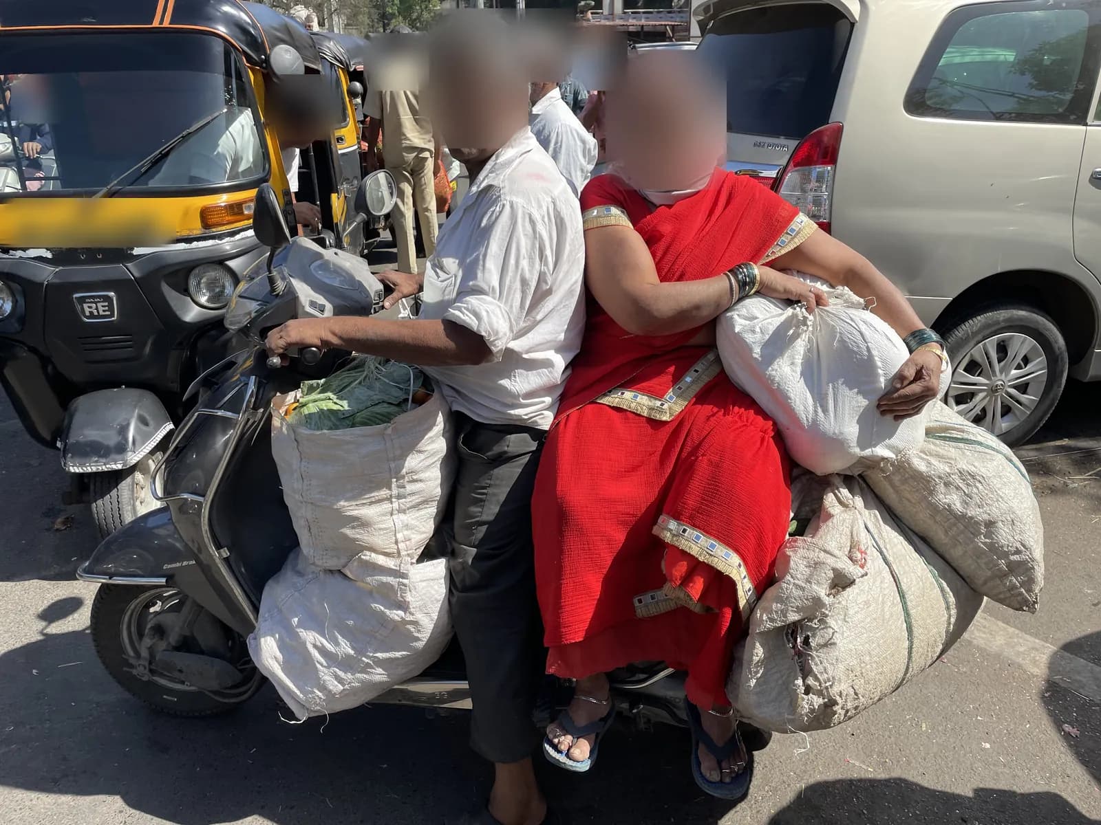 An older couple on a scooter, the woman holding a sack on her lap with more sacks tied on