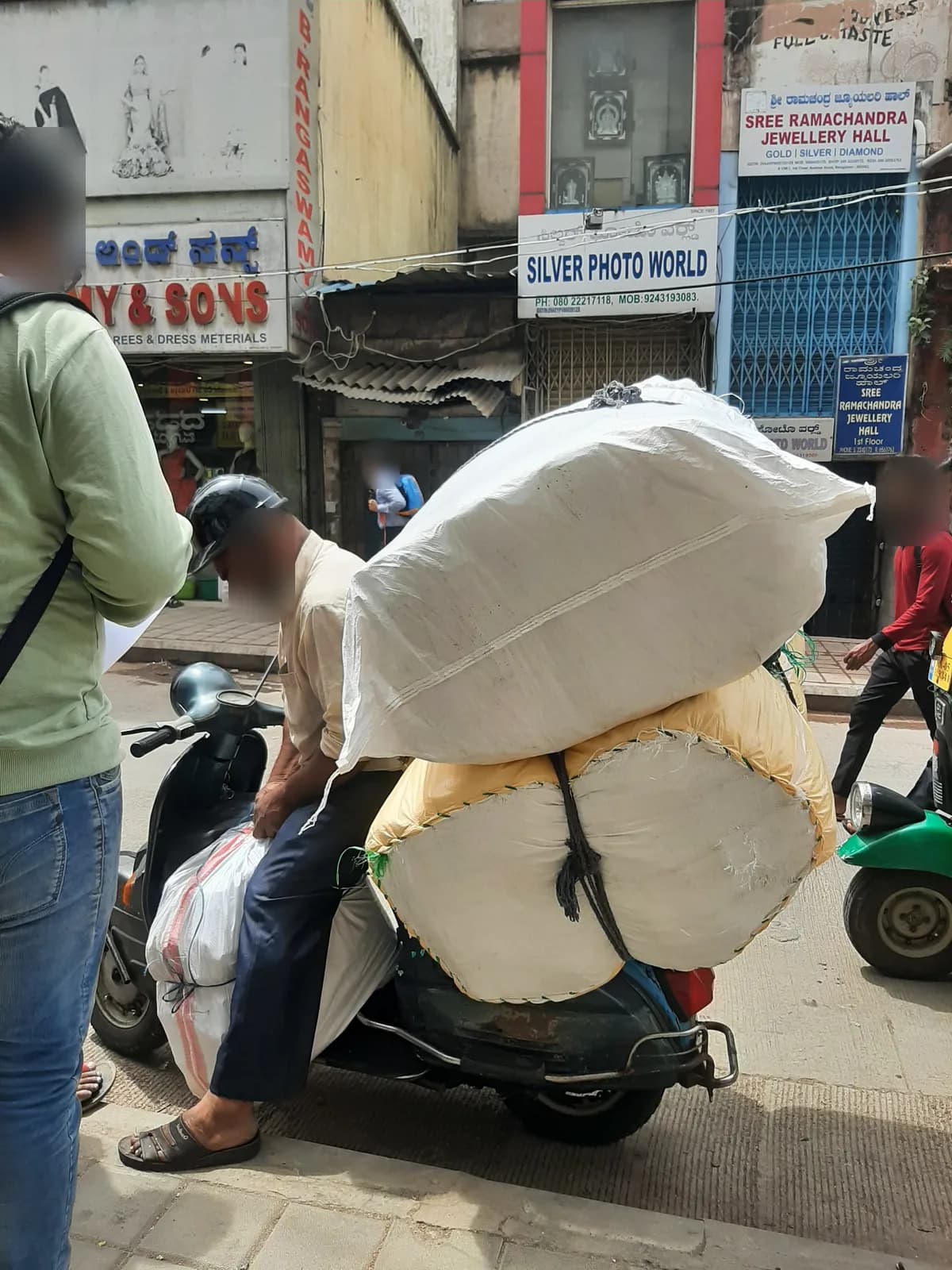 A rider on a scooter with two huge white sacks stacked behind him on a busy shopping street