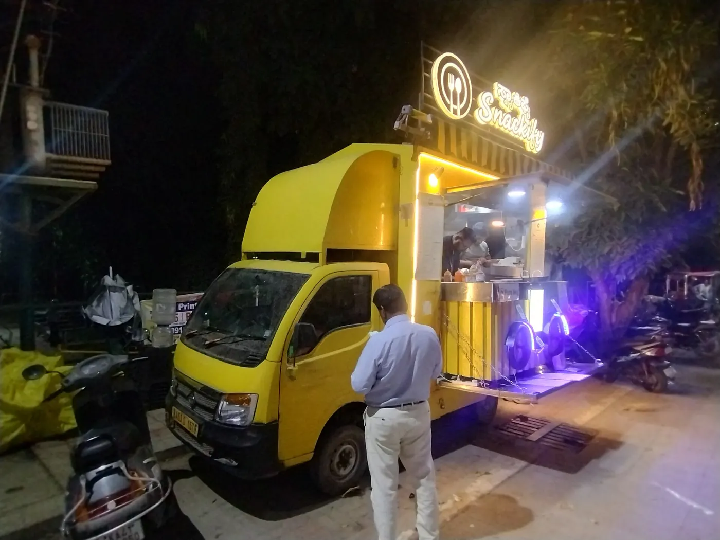 A yellow food truck lit up at night with a customer at its counter