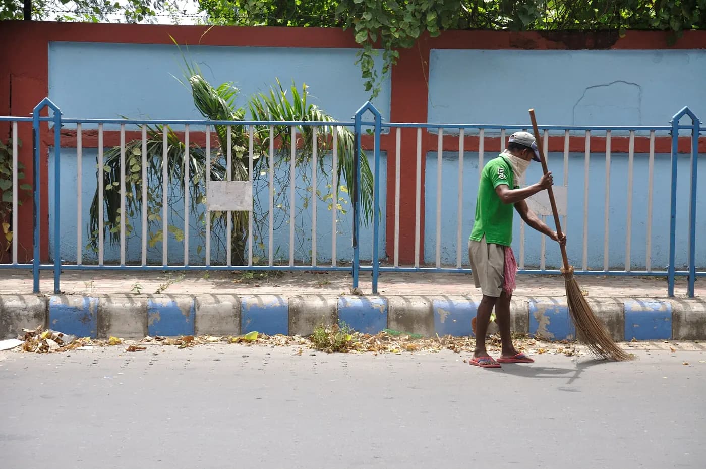 A sweeper with a long broom cleaning the edge of a footpath beside a railing