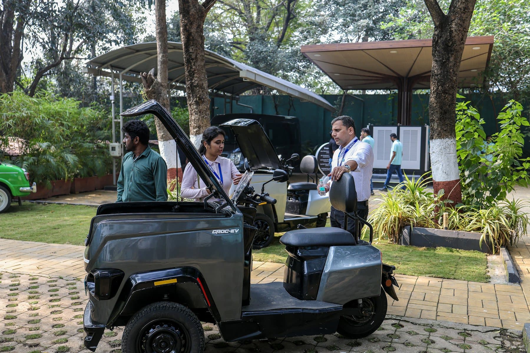 Visitors at an outdoor expo look over a graphite CROC EV with its cargo box lid open, with a white CROC EV parked behind it.