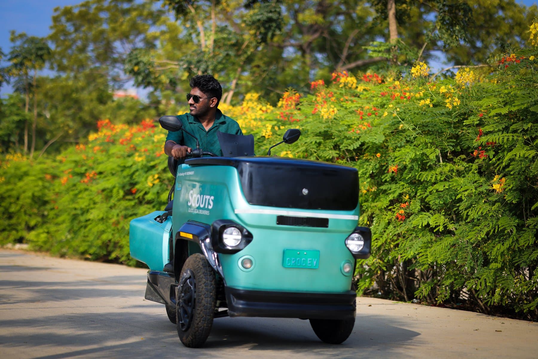 A teal CROC EV on a road lined with flowering trees